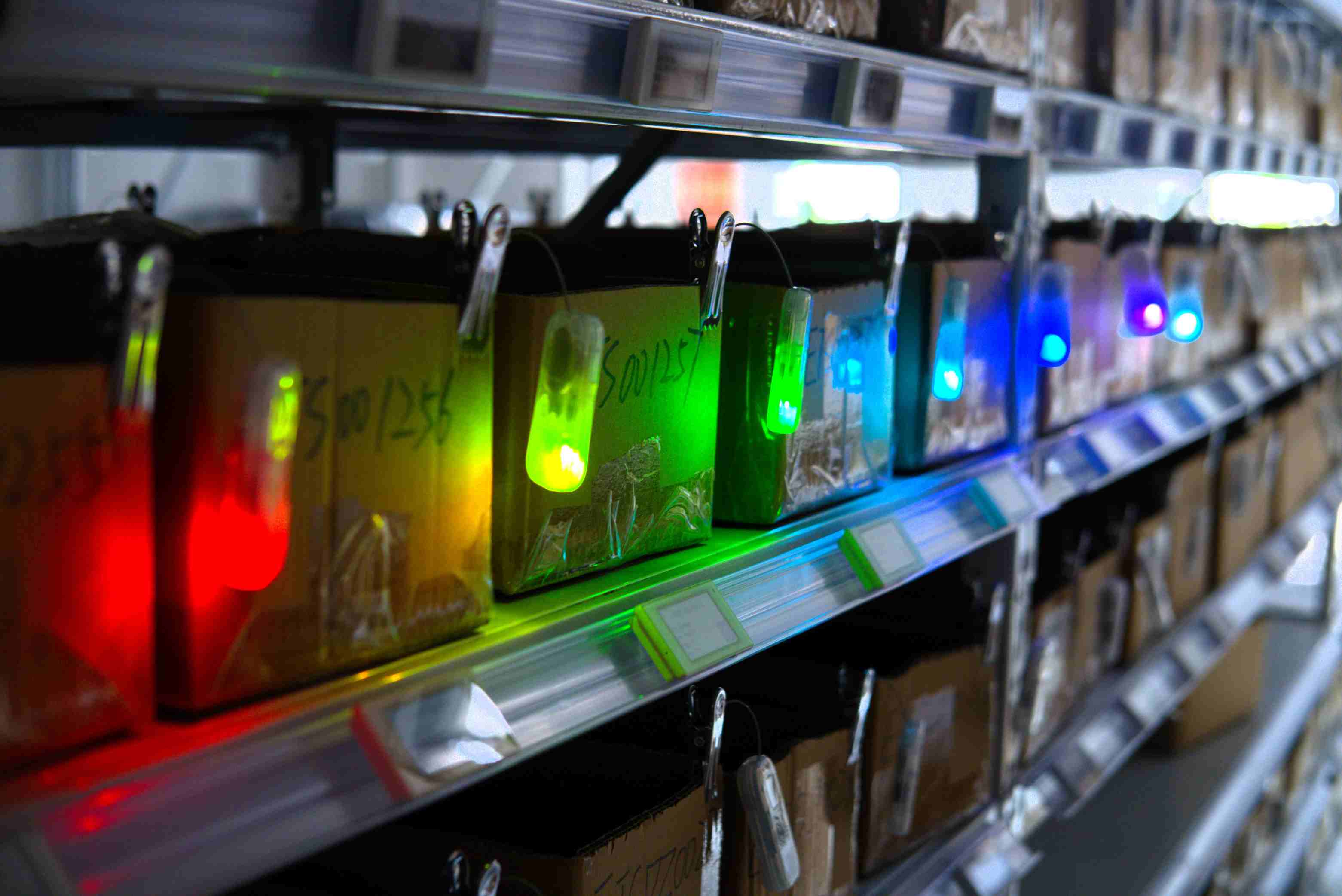 A worker finding a package instantly in a dense warehouse shelf guided by a flashing green LED light on a smart finding tag.